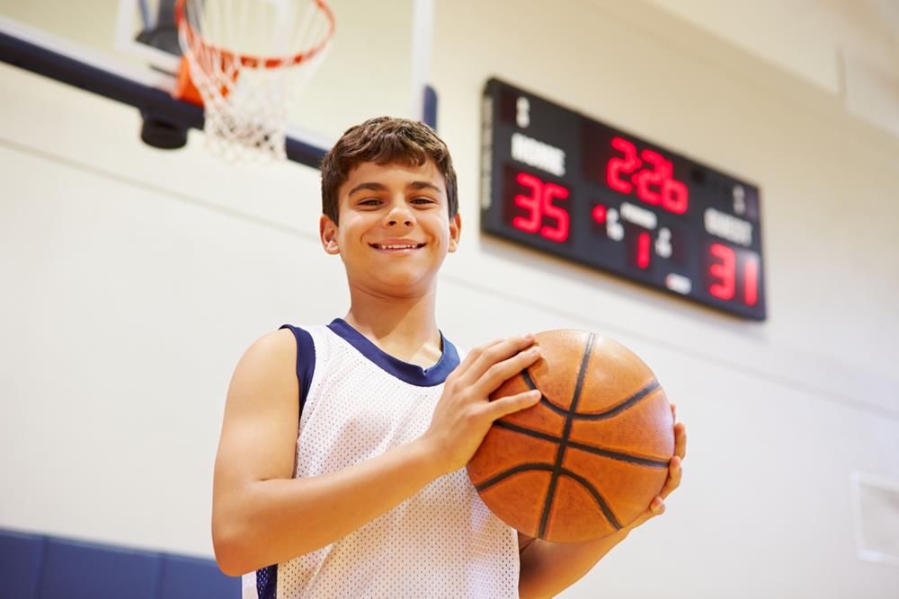 A male high school basketball player inside the gym, smiling while holding basketball
