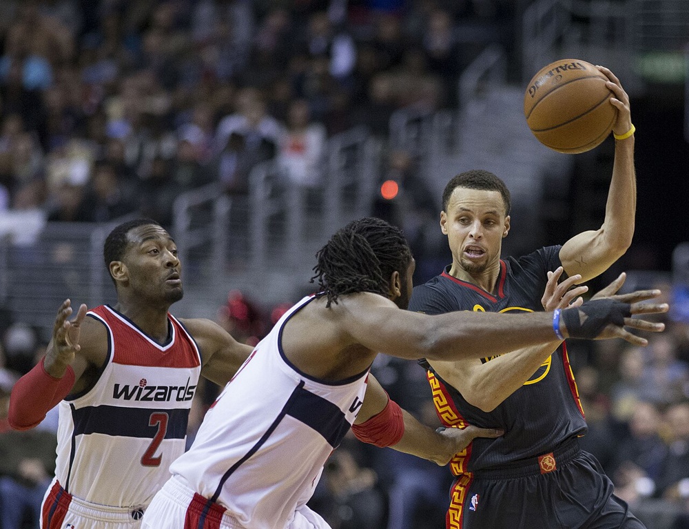 Curry attempting a pass while being guarded by John Wall and Nenê. Curry averaged 7.7 assists per game during the 2014–15 regular season, the sixth-highest in the league