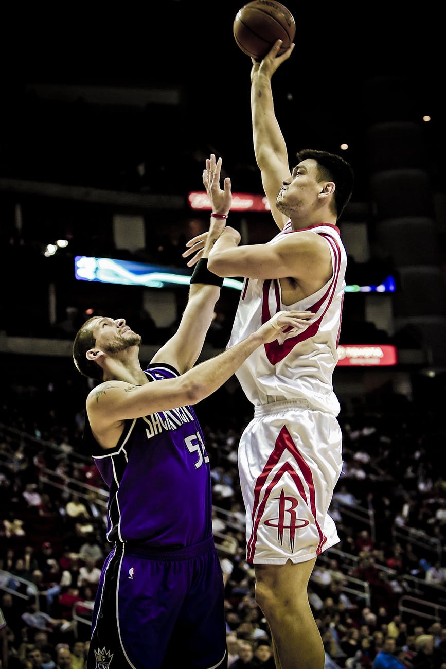 yao ming holding basketball on his left hand while jumping