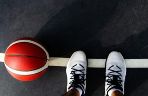 basketball player with his feet on the black court and an orange ball next to him. he is stepping on a white line. ready for the game.