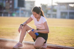 Asian Sports women using freezing spray for treating injured sportwomen's knee and leg after run