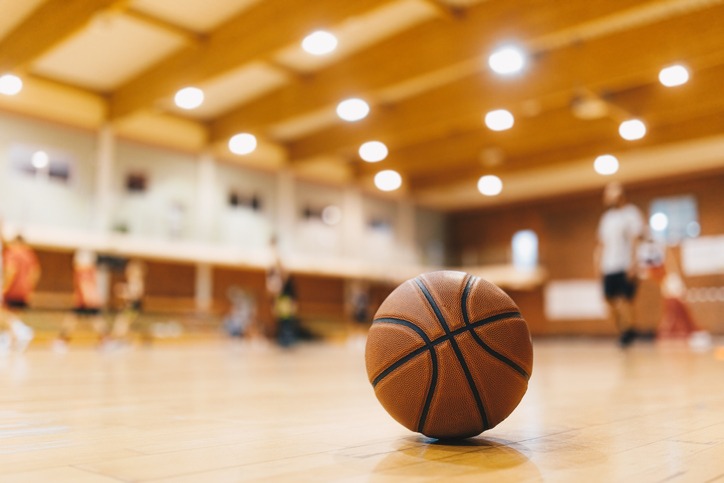 Basketball Training Game Background. Basketball on Wooden Court Floor Close Up with Blurred Players Playing Basketball Game in the Background