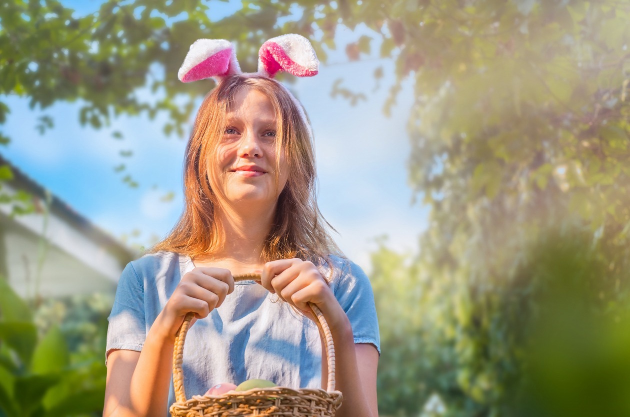 Portrait-of-a-teenage-girl-in-bunny-ears-with-an-Easter-basket-with-eggs-in-the-backyard