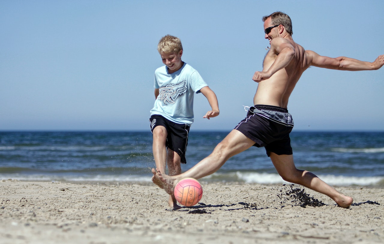 Man and boy playing soccer on the beach
