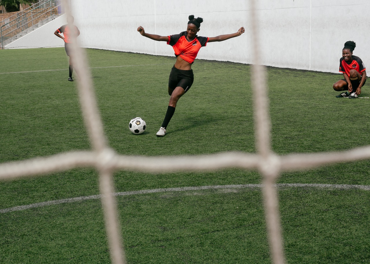 girl in a red shirt and black shorts kicking a soccer ball
